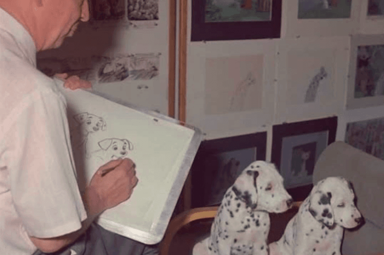An animator sketches Dalmatian characters while two dogs watch.